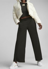 Weißer Daunenjacke mit hohem Kragen, schwarzem Cropped Top und weit geschnittenen schwarzen Hosen. Weiße Sneakers mit farblichen Akzenten. Matte Texturen.