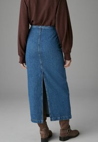 Denim maxi sukně s rozparkem na zádech, vysokým pasem a tradiční modrou texturou látky. Spárováno s hnědými kotníkovými botami.