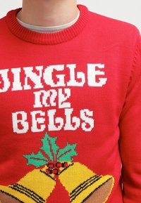 Pull rouge tricoté avec le texte blanc « JINGLE MY BELLS », orné de cloches jaunes, de feuilles de houx vertes et d'un ruban à carreaux noirs.