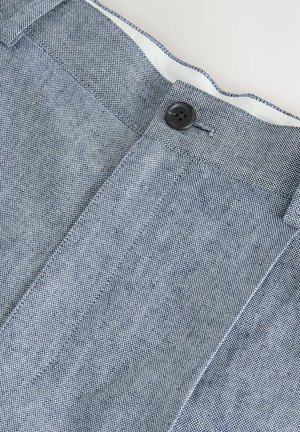 Zbliżenie na niebiesko-białe, strukturalne spodnie materiałowe z czarnym guzikiem i widoczną podszewką paska.