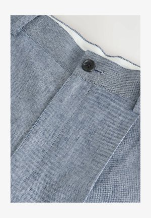 Zbliżenie na niebiesko-białe, strukturalne spodnie materiałowe z czarnym guzikiem i widoczną podszewką paska.