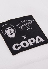 Wit kledinglabel met een zwarte rechthoek. Het label bevat een monochrome portret, de tekst "Diego", een met de hand getekende handtekening en het "COPA" logo.