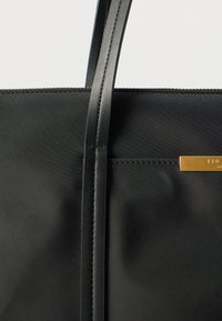 Μαύρη τσάντα ώμου με απαλό υφασμάτινο φινίρισμα, δύο λεπτές λαβές, μεταλλικά στοιχεία σε χρυσό τόνο για αντίθεση και τσέπη στο πλάι ως διακοσμητικό στοιχείο.