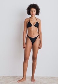 Svart bikini-sett med trekantet bh med tynne stropper og matchende lavt liv bukse; glatt tekstur, minimalistisk design.