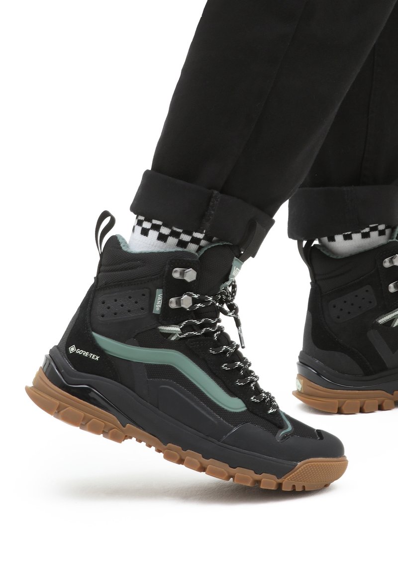 Czarno-zielone wysokie buty górskie z teksturowaną cholewką, grubą gumową podeszwą i wzorzystymi sznurówkami; wyposażone w Gore-Tex dla wodoodporności.