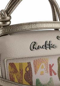 Beige strukturierte Handtasche mit einem metallisch silbernen Griff und einem farbenfrohen abstrakten Design mit Alphabetmustern und dekorativen Akzenten.