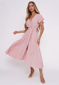 Helles rosa Wickelkleid mit tiefem V-Ausschnitt und kurzen schwingenden Ärmeln. Es verfügt über einen Bindegürtel in der Taille und einen seitlichen Schlitz für Bewegungsfreiheit.