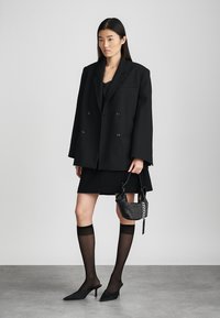 Μαύρο υπερμεγέθη διπλό πανωφόρι συνδυασμένο με μαύρη φούστα, διάφανες μαύρες κάλτσες μέχρι το μηρό και μυτερά μαύρα τακούνια. Μικρή υφασμάτινη τσάντα.