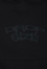 Schwarzer Stoff mit dezent gesticktem abstraktem Design in einem etwas dunkleren schwarzen Faden, der ein strukturiertes Muster in der Mitte erzeugt.