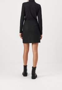 Minifalda negra ajustada con una textura suave. Se lleva con una blusa negra de manga larga que presenta un sutil patrón ondulado y se combina con botas negras gruesas.