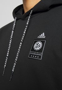 Svart hoodie i bomullsblandning, med en vit logotyp och broderat varumärke. Har dragsnören med textdetaljer.