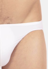 Weißer Slip aus glattem, elastischem Stoff, der eine einfarbige und minimalistische Gestaltung aufweist. Der Bund ist elastisch und schmiegt sich flach an die Haut.