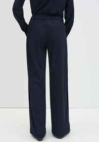 Donkerblauwe wijde broek met een elastische taille, gladde stof en een enkele achterzak. Platte naden en een ontspannen pasvorm zorgen voor extra comfort.