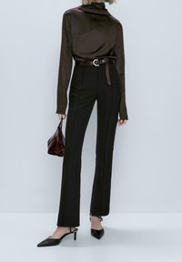 Col roulé en satin marron, pantalon noir taille haute et ajusté, escarpins noirs à bout pointu, et un petit sac à main bordeaux.