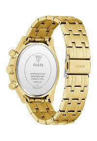 Montre en acier inoxydable doré au design épuré, avec un cadran rond et un bracelet ajustable, montrant l'arrière avec des détails de marque.
