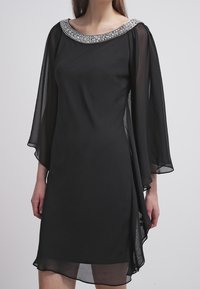 Robe en chiffon noir avec manches cloche, encolure argentée ornée, design fluide, et longueur au-dessus du genou. Sans motifs ni détails métalliques.