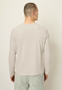 Dlhý béžový rukáv s okrúhlym výstrihom, vyrobený z mäkkej tkaniny, v kombinácii s textúrovanými svetlozelenými kordovými nohavicami.