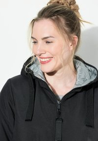 Schwarze Kapuzenjacke mit grauem Innenfutter, ausgestattet mit einem Reißverschluss, einer verstellbaren Kapuze und strukturiertem Stoff. Ideal für Freizeitkleidung.