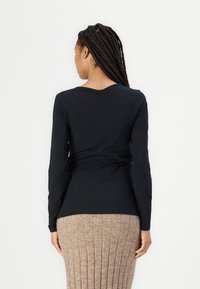 Langermet svart topp i mykt stoff, med rund hals og tettsittende design, kombinert med en ribbestrikket beige skjørt.