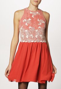 Červené šaty s těsným korzetem a bílou květinovou výšivkou, vyznačující se splývavou sukní. Vyrobeny z lehké látky, s halter krkem.