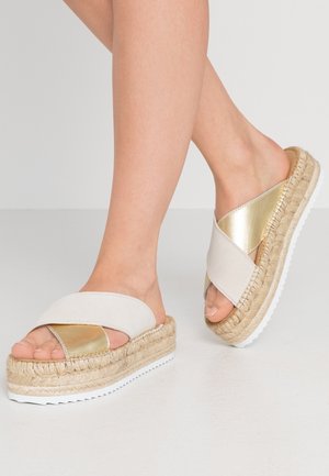 Jasnobeżowe espadryle wsuwane z metalicznym, złotym akcentem, grubą plecioną juty podeszwą i fakturowaną białą gumową podeszwą zewnętrzną.