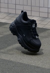 Schwarzer Sneaker mit einer klobigen Sohle, Obermaterial aus glattem Leder, runder Zehenform, Schnürung auf der Vorderseite und Markenlogo an der Seite und auf der Zunge.