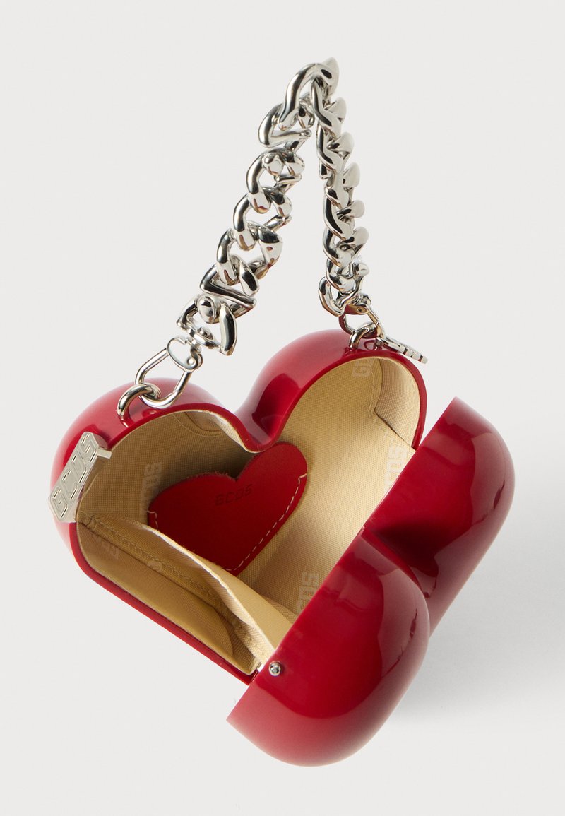 Rød hjerteformet håndtaske med en blank finish, der har et sølvfarvet kædehåndtag og beige indvendig, inklusive en lille hjerteaccent.