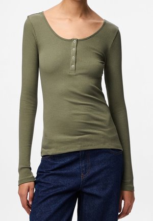 Slim fit geribbeld olijfgroen top met lange mouwen, ronde halslijn en vierknopensluiting, gecombineerd met donkerblauwe denim jeans.