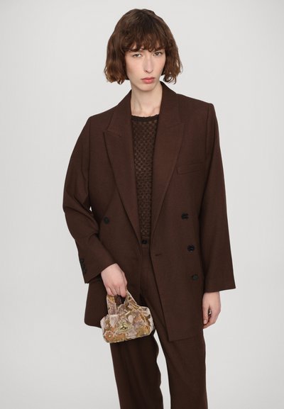 Brown, oversized blazer with double buttons, paired with a textured knit top and matching trousers; holding a small, patterned handbag.