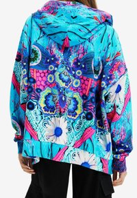 Bluza z kapturem w jaskrawych kolorach niebieskim, różowym i fioletowym, zdobiona kwiatowymi i motyli wzorami. Charakteryzuje się luźnym krojem i miękką fakturą.