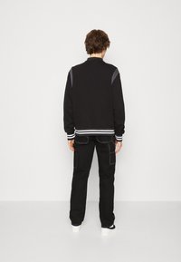 Svart sweatshirt med kontrasterande grå axelaccenter, ribbade handleder och fåll; parat med svarta cargobyxor med vit söm.