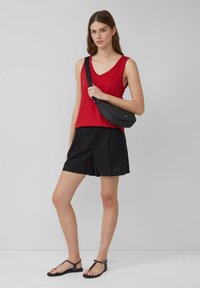 Rode mouwloze top, zwarte geplooide shorts, zwarte riemtas en platte zwarte sandalen. Glad stof, ontspannen pasvorm en minimalistisch ontwerp.