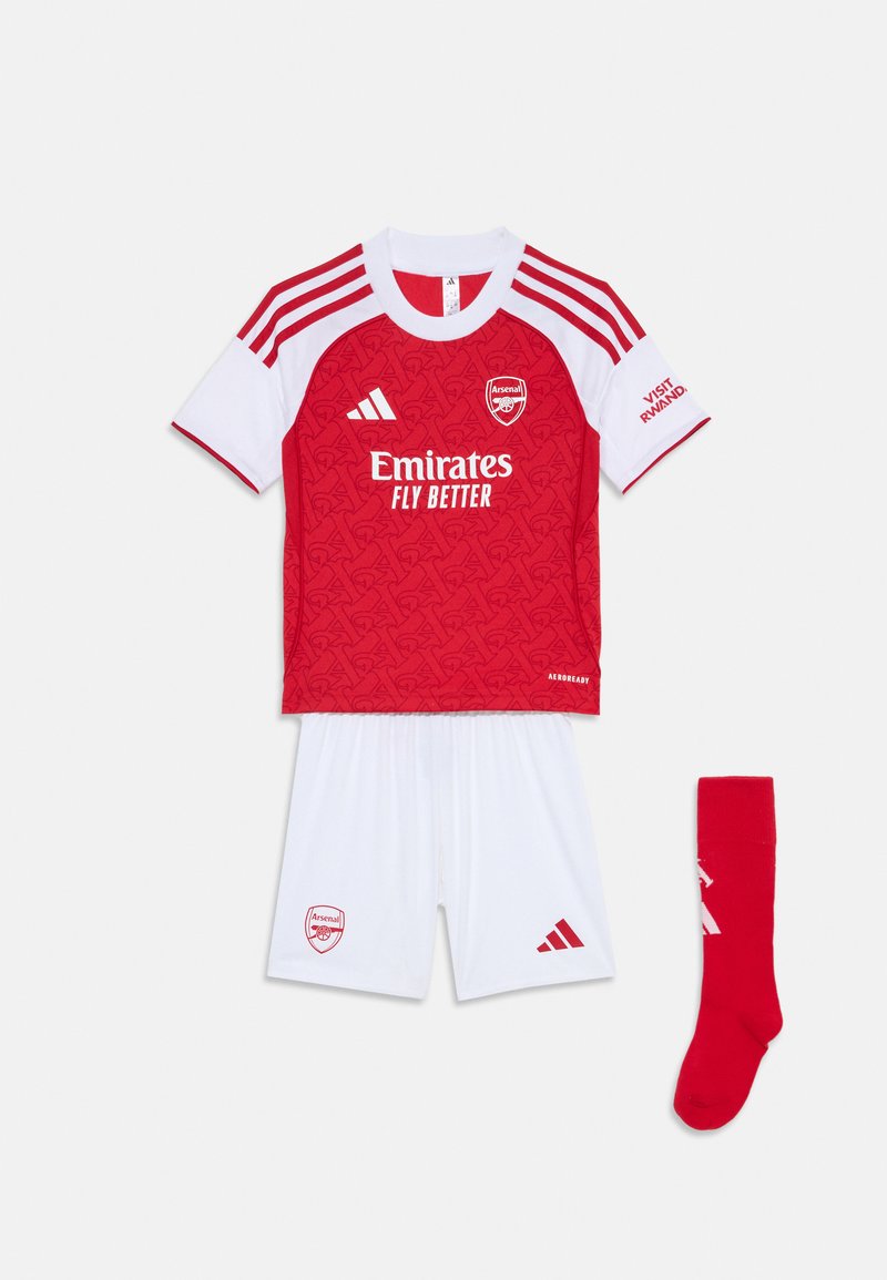 Conjunto de fútbol juvenil en rojo y blanco que incluye una camiseta de manga corta con un patrón texturizado, pantalones cortos blancos y un calcetín rojo con detalles blancos.