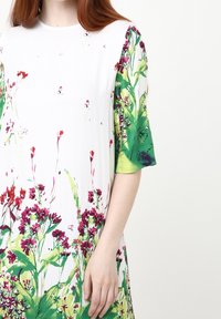 Vestido floral con base blanca y estampados botánicos en verde y purpura, mangas cortas y un corte relajado. Textura de tela suave.