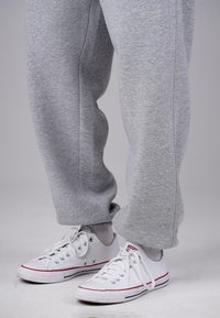 Legs wearing gray sweatpants and white low-top Converse sneakers with red and blue stripes against a light gray background.