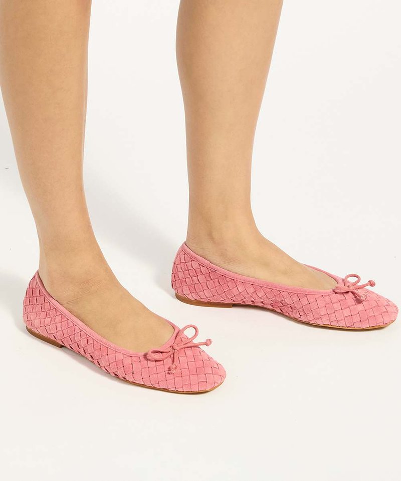 Deux pieds portant des ballerines tissées roses avec de petits nœuds sur le dessus, sur un fond blanc.