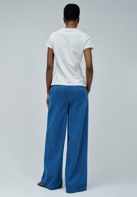 Camiseta blanca de manga corta combinada con jeans de pierna ancha azules. Los jeans tienen un diseño clásico de cinco bolsillos y un corte recto.
