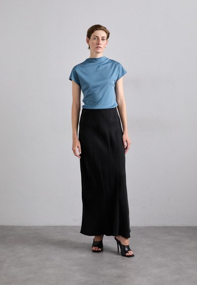 Lys blå tettsittende topp med korte ermer, pyntet med et svart maxikjole. Modell med svarte sandaler med åpen tå. Jevne teksturer, minimalistisk design.