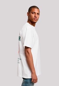 Witte katoenen t-shirt met ronde hals en korte mouwen. Kenmerkt zich door een grafische print in groen en rood op de achterkant, een relaxte pasvorm en zijnaaddetails.