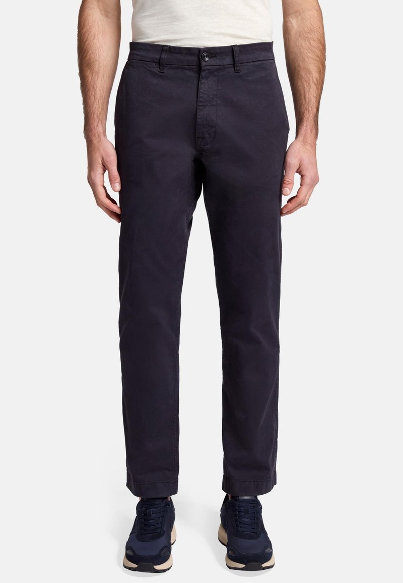 Granatowe spodnie wykonane z tkaniny bawełnianej, o prostym kroju, z kieszeniami z przodu i zapięciem na guzik, zestawione z ciemnymi trampkami.