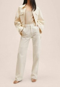 Beżowa koszula z denimu z długimi rękawami i kieszeniami z przodu, zestawiona z kremowymi spodniami z wysokim stanem. Gładka faktura, luźny krój, minimalistyczny design.