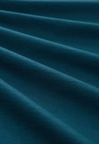 Teal stof med en glat tekstur, der har subtile rynker og folder, som fremhæver sin elasticitet og rige farvedybde.