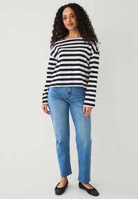 Zwart-wit gestreepte blouse met lange mouwen, gecombineerd met blauwe rechte jeans en zwarte platte schoenen. Eenvoudig, casual ontwerp met een relaxte pasvorm.