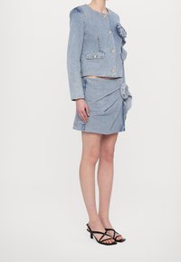 Kurtka dżinsowa ze złotymi guzikami, falbaną i dwoma kieszeniami, zestawiona z pasującą spódnicą o plisowanym fasonie i kwiatowym akcentem.