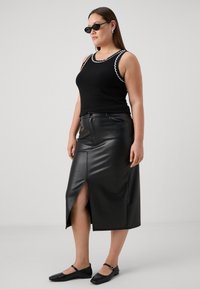 Top in cotone nero a coste con bordi bianchi a scallop, abbinato a una gonna in pelle nera a vita alta con spacco frontale. Scarpe flats nere completano l'outfit.