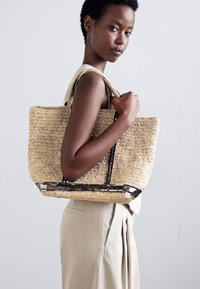 Torebka z plecionego słomy o prostokątnym kształcie, z czarnym wykończeniem wzdłuż górnej krawędzi i teksturowaną powierzchnią dla dodatkowego efektu.