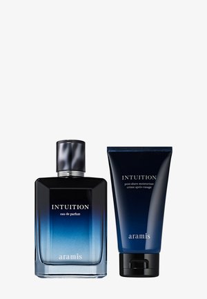 Ensemble de parfum Intuition comprenant une bouteille en verre carré avec un dégradé de bleu et un capuchon argenté, accompagnée d'un tube de crème bleu foncé.