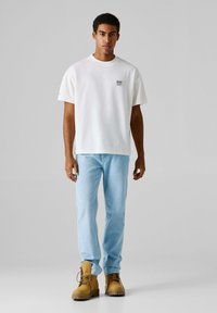 Λευκό βαμβακερό μπλουζάκι με κοντά μανίκια, με ένα μικρό γραφικό στο στήθος. Ανοιχτό μπλε τζιν παντελόνι και καφέ μποτάκια με κορδόνια ολοκληρώνουν το ντύσιμο.