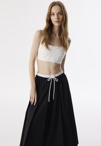 Witte cropped top van textuurstof en zwarte, hoge taille rok met een elastische tailleband en witte trekkoord.
