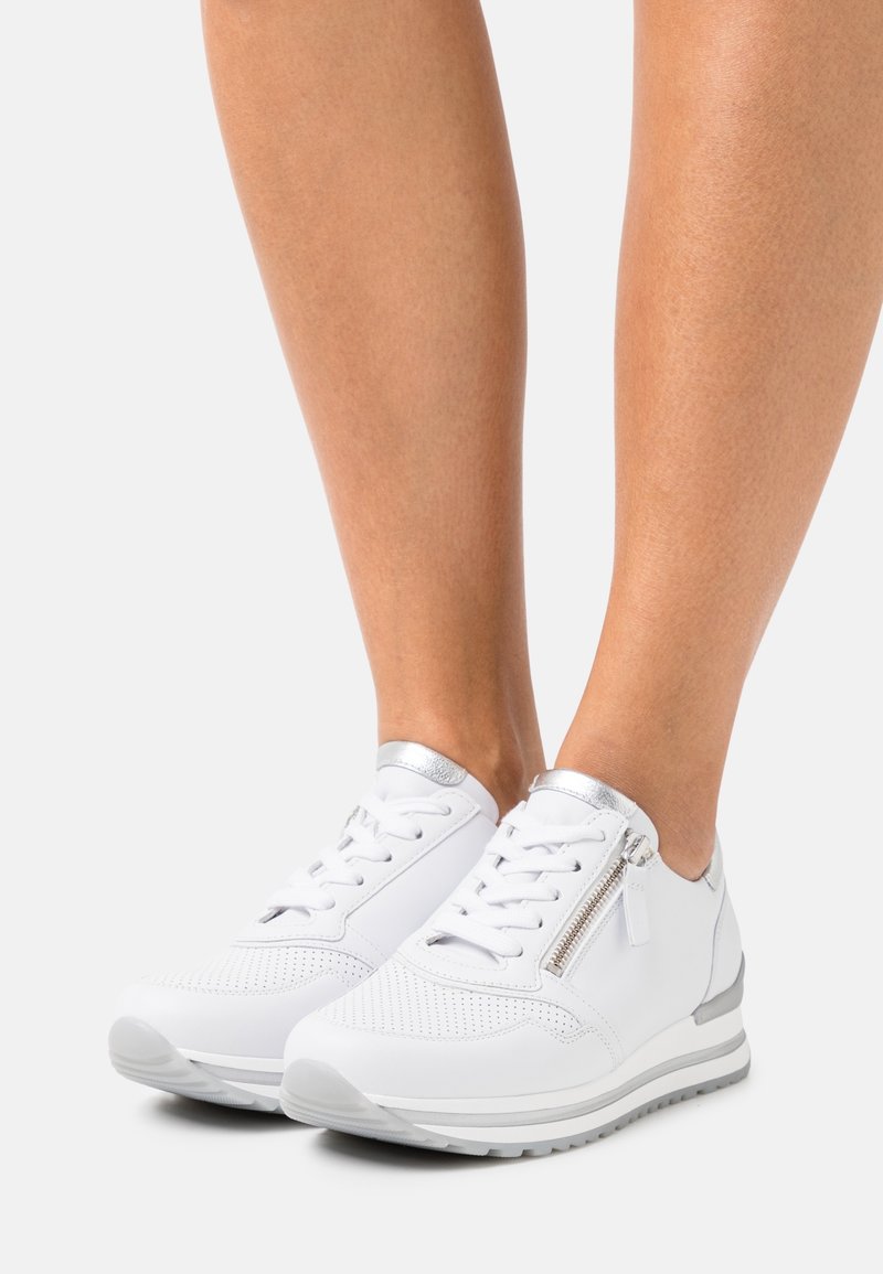 Vita sneakers med perforerad design, silveraccents, sidovy kedja och texturerad gummisula. Rundad tå och vadderad krage.